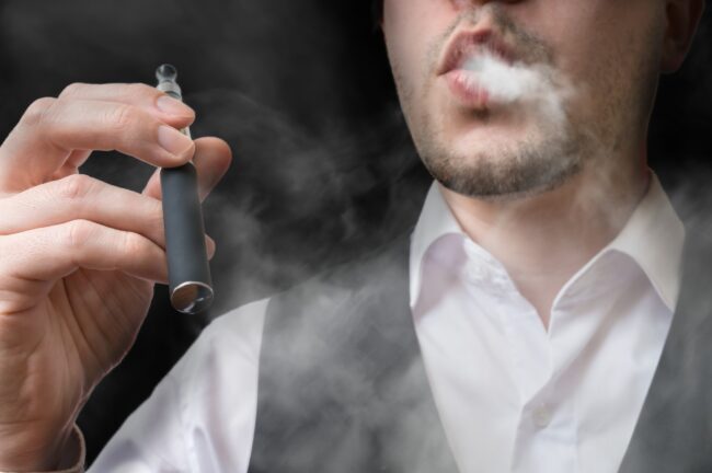 Man vaping electronic cigarette and blowing smoke.