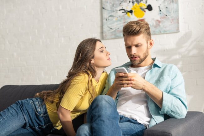 Attractive girl looking at dependent boyfriend with smartphone on couch